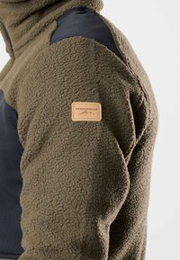 Fleece jack in olijfgroen, met zwarte nylon accenten op de schouders. Bevat een tan leren label met het "SWEDEMOUNT" logo. Geweven oppervlak.