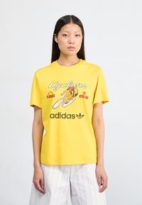 Yellow cotton t-shirt featuring a bicycle graphic and the text "Cyclone" and "Adidas" in a retro font. Short sleeves, crew neck design.