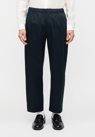 Pantalon bleu marine avec une ceinture élastique, coupe droite et tissu léger, associé à des mocassins noirs et des chaussettes blanches.