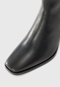 Black leather ankle boot with a pointed toe, smooth texture, and a low heel. Features a sleek design and minimal stitching detail.