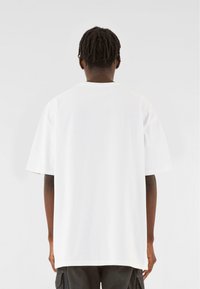 Hvid bomulds T-shirt med korte ærmer, rund halsudskæring og en afslappet pasform, set fra ryggen. Minimalistisk design, ingen synlige mønstre.
