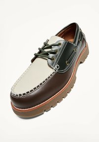 Bőr mokaszin stílusú cipő barna, krémszínű és sötétzöld panelekkel, zöld fűzőkkel, varrással díszítve, vastag gumitalppal.