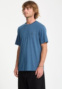 Kortærmet, blå t-shirt i et blødt, tekstureret stof med rund halsudskæring og lille sort logo på venstre bryst. Matchet med sorte bukser.