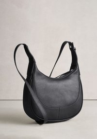 Sac bandoulière en cuir noir texturé avec une sangle d'épaule réglable et un panneau avant courbé, sur un fond clair et neutre.