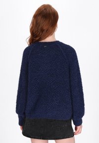 Navy blue textured knit sweater with a round neckline, drop shoulders, and ribbed cuffs, paired with a black denim mini skirt.