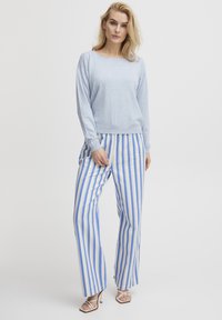 Maglione di cotone azzurro chiaro con scollatura ampia, abbinato a pantaloni a vita alta a righe blu e crema. Tacchi con cinturini completano il look.