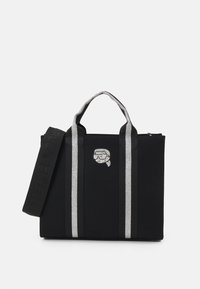 Borsa tote in tela nera con strisce argento, manici robusti e chiusura con zip. Presenta una grafica decorativa sulla parte anteriore.