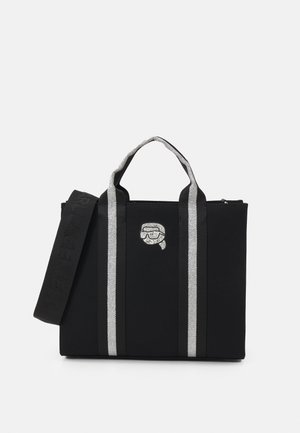 Black canvas tote bag with silver stripes, sturdy handles, and a zip closure. Features a decorative graphic on the front.