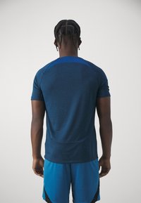 Kortärmad sporttröja i mörkblått tyg med ett strukturerat mönster och släta axeldetaljer, kombinerad med blå shorts.