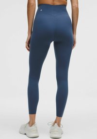 Marina blå högmidjade leggings i stretchigt material, med en mjuk yta och minimalistisk branding, kombinerat med vita träningsskor.
