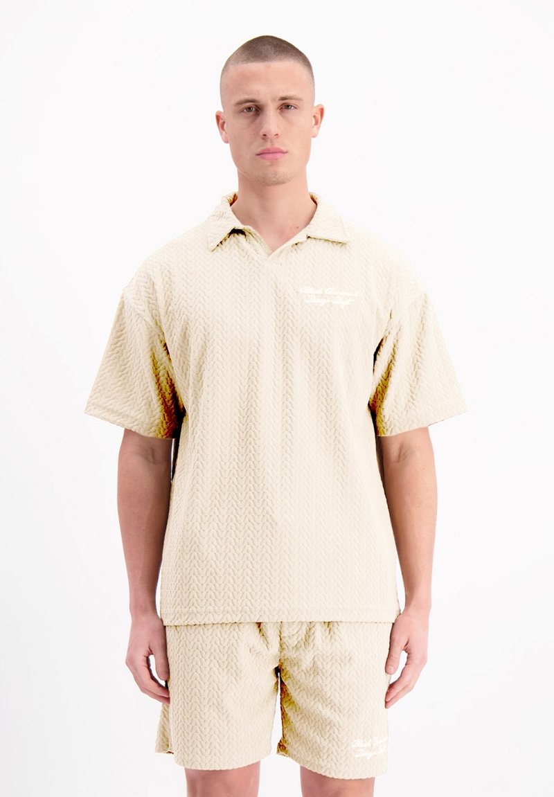 Beige kortekoortshirt en bijpassende shorts met een gestructureerd zigzagpatroon. Voorzien van een kraag en subtiele logodetails.