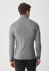 Top gris de manga larga con cuello alto, hecho de una tela suave. El diseño presenta un ajuste ceñido y una textura sutil, combinado con jeans oscuros.