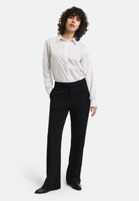 White button-up shirt with black polka dots, paired with black tailored trousers and pointed black shoes, featuring a relaxed fit and smooth texture.