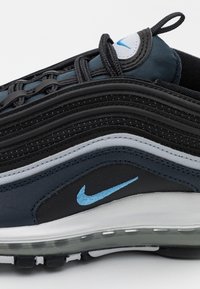 Zapatilla Nike Air Max 97 con un upper texturizado en negro y azul, acentos grises y una unidad de amortiguación de aire visible en la suela.