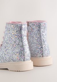 Sølvglitrende ankelstøvler med pink detaljer, der har en glat overflade, rund tå og beige gummisåler.