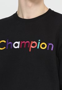 Černá mikina s nápisem "Champion" vyšitým v barevných písmenech. Klasický kulatý výstřih a krátké rukávy.