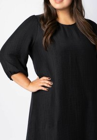 Schwarzes, strukturiertes Kleid mit dreiviertel Puffärmeln und rundem Halsausschnitt, das ein zartes Crinkle-Muster und eine lockere Passform aufweist.