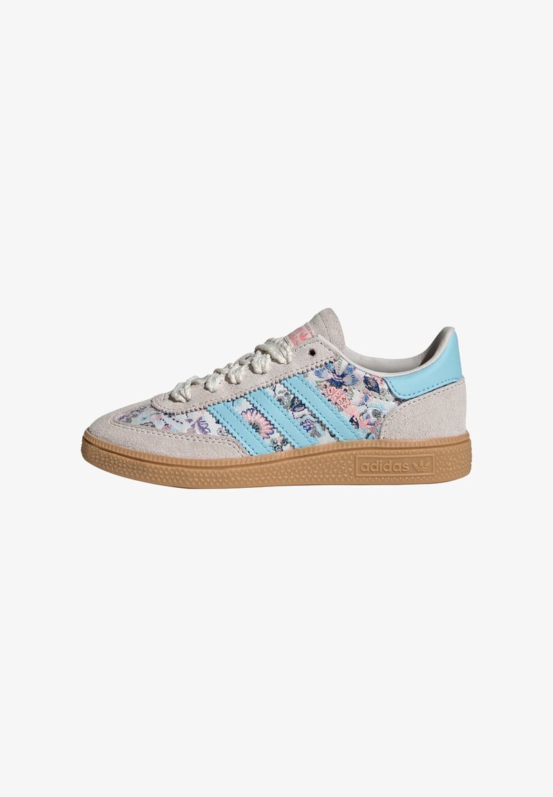 Baskets basses Adidas en daim beige, avec des rayures bleues, un motif floral sur les côtés en tissu, une semelle en gomme et une fermeture à lacets.