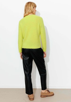 Pull texturé vert citron vif à manches longues, associé à un pantalon en similicuir noir et des chaussures marron à lacets. Vue de dos.