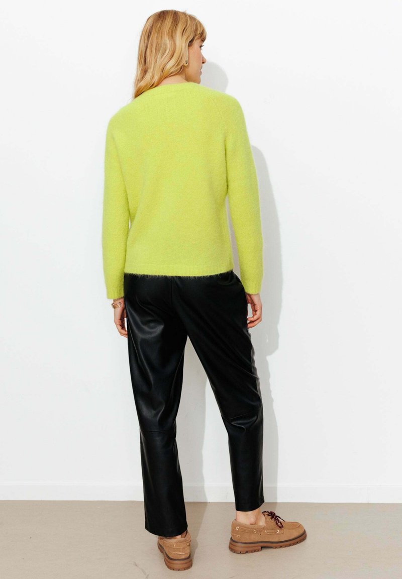 Pull texturé vert citron vif à manches longues, associé à un pantalon en similicuir noir et des chaussures marron à lacets. Vue de dos.