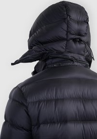 Personne portant une doudoune noire brillante avec la capuche relevée, vue de dos, montrant une fermeture éclair et un cordon sur la capuche.