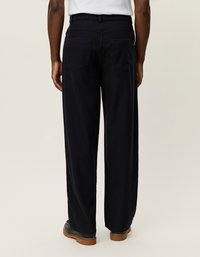 Μαύρο παντελόνι σε φαρδιά γραμμή με ψηλή μέση, διαθέτοντας δύο πίσω τσέπες και υφάσματος με λεπτή υφή. Συνδυάζεται με μαύρα υποδήματα.