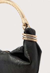 Crna strukturirana kožna torba u kutu s detaljima zlatnog i srebrnog prstena te zlatnim ručnim dodatkom s teksturom krokodila.