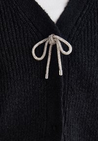 Cardigan negru tricotat cu design în formă de V, cu o închidere la față sub formă de fundiță din mărgele argintii, material texturat și model canelat.