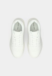 Baskets blanches en cuir lisse, dotées d'une semelle rembourrée, d'une zone des orteils perforée et de lacets plats. Nom de la marque imprimé à l'intérieur de la languette.