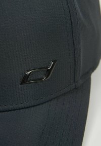 Czarna czapka wykonana z teksturowanej tkaniny z zakrzywionym daszkiem. Posiada błyszczący czarny akcent logo po bokach. Haftowane detale wzdłuż szwów.