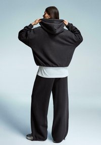 Przyduży czarny hoodie z wysokim kołnierzem i dużym kapturem, w połączeniu z luźnymi czarnymi spodniami i białą podkoszulką. Miękka tekstura materiału.