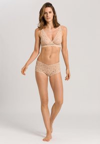 Värihihnoilla varustettu pitsinen bralette ja siihen sopivat hipster-shortsit vaaleassa beigevässä. Sisältää kukkakuvioita, kaarevia reunoja ja joustavaa, läpinäkyvää kangasta.