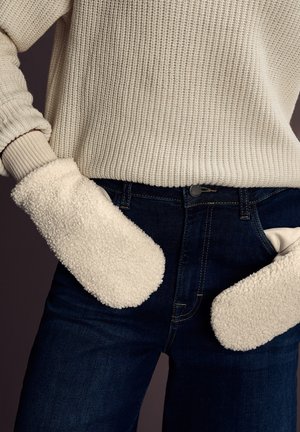 Hvide fleecevanter med en tekstureret overflade, der har ribbede manchetter, parret med mørke denimjeans og en lys strikket sweater.