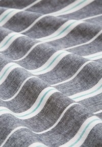 Grå stof med en tekstureret vævning, der har bølgede striber i hvid og teal. Mønsteret skaber en dynamisk visuel strøm gennem materialet.