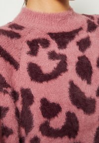 Pull doux rose pâle en tissu duveteux avec un grand motif abstrait de léopard violet foncé, visible de la poitrine supérieure jusqu'au cou.