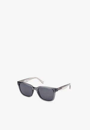 Gafas de sol con un marco rectangular, material opaco de color gris oscuro, lentes tintados y varillas transparentes con sutiles detalles a rayas.