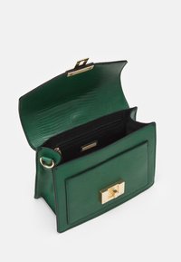 Sac à main en cuir texturé vert avec fermoir doré, rabat ouvert et doublure intérieure noire montrant une poche zippée et un compartiment intérieur.