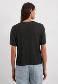 Zwart T-shirt met korte mouwen, ronde halslijn, iets losse pasvorm en een gladde textuur. Draagt met lichtblauwe cargobroek.
