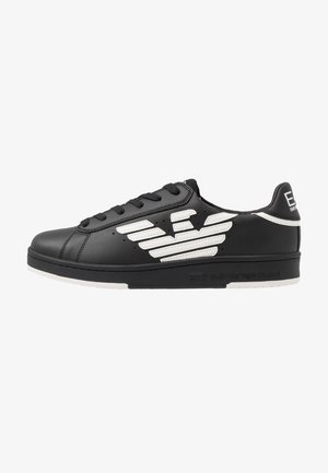 Zapatillas de cuero negro con detalles en blanco, que presentan un logo en forma de ala, puntera redonda y suela de goma plana, diseñadas con cordones y detalles perforados.
