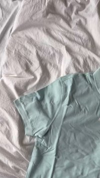 Licht turquoise polo-shirt gemaakt van zachte, gestructureerde stof, met een klassieke kraag en korte mouwen, gedeeltelijk over een witte ondergrond gedrapeerd.