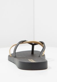 Tongs noires avec une semelle en caoutchouc texturé, munies de fines sangles dorées et d'un entre-doigts en forme de Y pour un meilleur maintien.