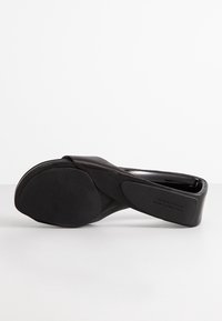 Scarpa nera slip-on con tomaia in pelle liscia e suola in gomma. Design curvo senza tacco. Presenta una texture morbida e un marchio discreto.