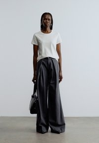 Biała koszulka z krótkim rękawem i okrągłym dekoltem, zestawiona z luźnymi, ciemnoszarymi spodniami o szerokich nogawkach. Dodatek: czarna torebka.