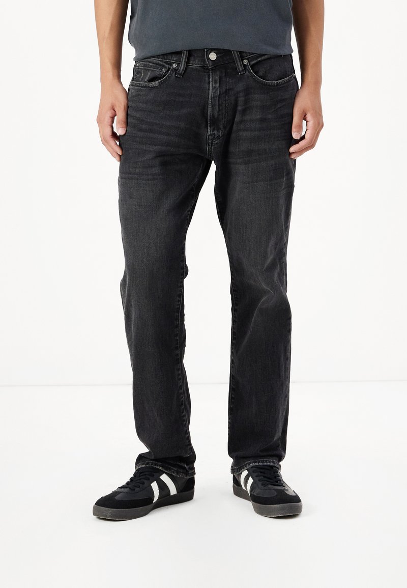 Jean en denim noir avec une coupe droite, dotés de poches avant et d'une fermeture à bouton classique. Portés avec des baskets noires.
