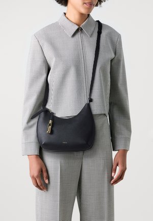 Borsa a spalla in pelle nera con forma curva, accessori in metallo dorato e superficie testurizzata. Indossata con un outfit monocromatico a fantasia.