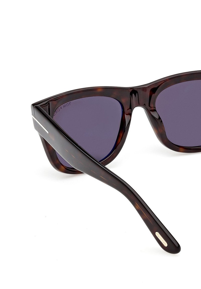 Lunettes de soleil œil-de-chat avec une monture en écaille de tortue, des verres violet foncé, et des branches élégantes et incurvées ornées d'un petit accent métallique.