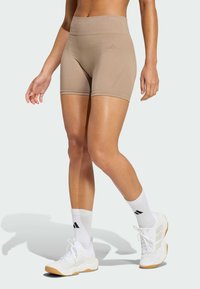 Tan high-waisted athletic shorts with a fitted design. Features subtle branding and smooth texture. Paired with white athletic socks and sneakers.