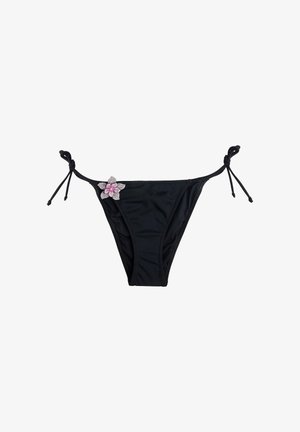 Slip bikini nero con fiocchi laterali e un fiore decorativo rosa e bianco sul lato sinistro.