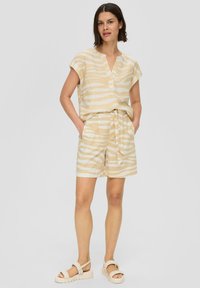 Beige kurzärmliges Oberteil und passende Shorts mit weißen Zebrastreifen. Mit V-Ausschnitt und Bindegürtel in der Taille. Strukturierter Stoff.