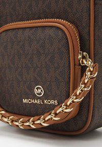 Borsa marrone Michael Kors con logo dorato, manico in pelle intrecciata e tracolla in catena dorata, e una cerniera visibile sulla tasca frontale.